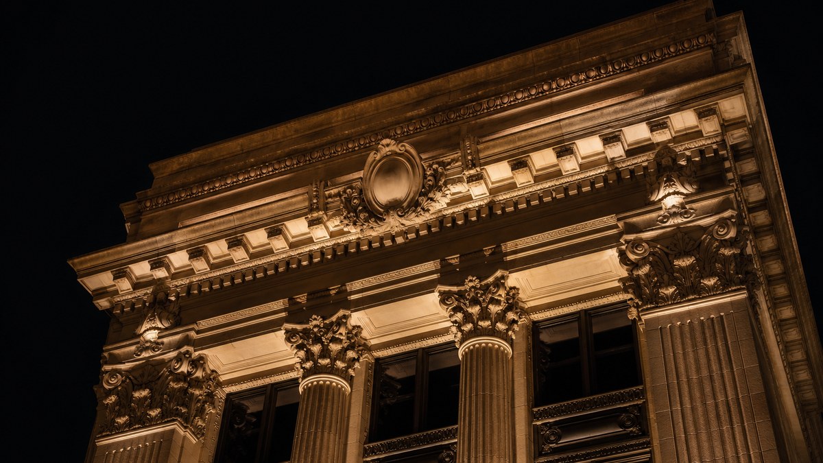 Historic limestone building cornice and columns in Fort Worth with warm LED accent lighting at night